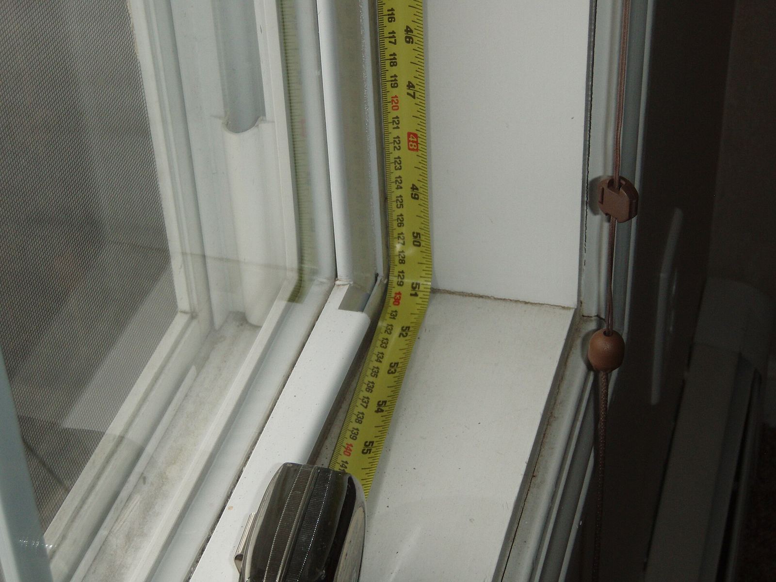 Gele rolmeter gespannen langs de vensterbank en het kader van een raam met dubbele beglazing